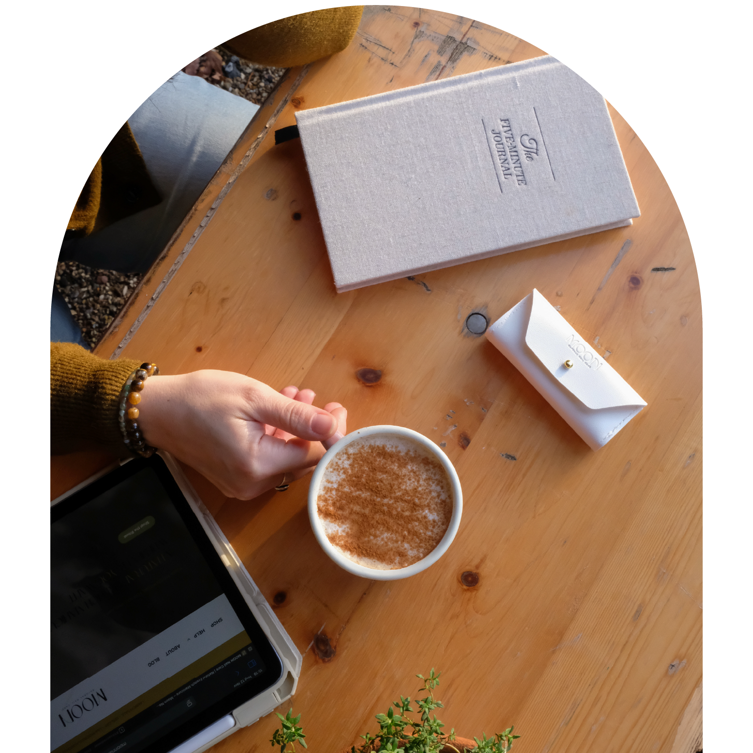 Woman holding a cup of coffee on a table with a journal, manicure kit and iPad