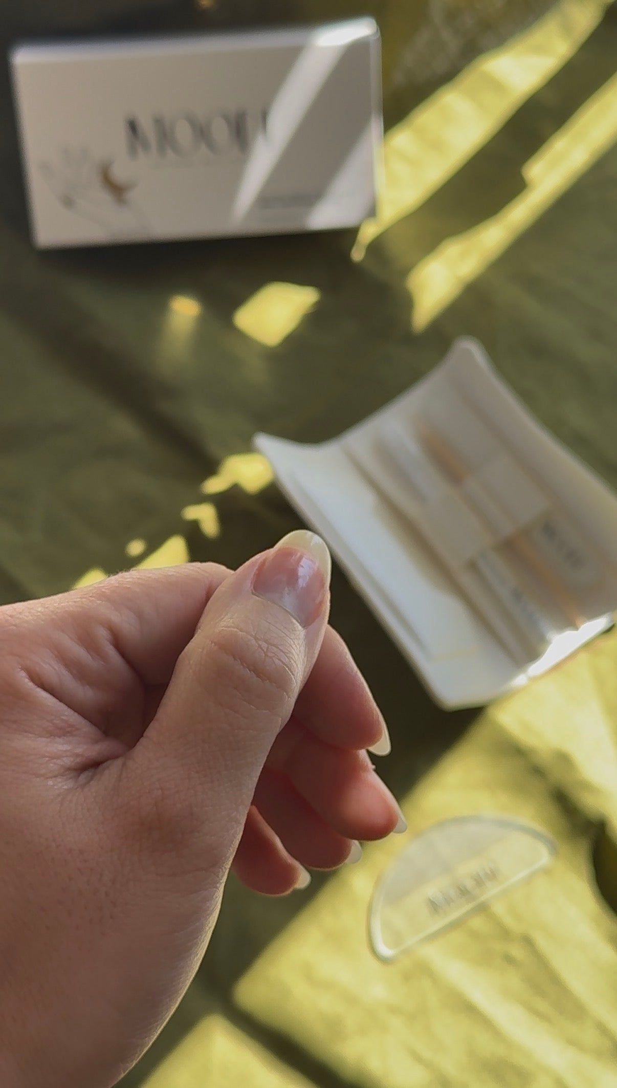 Hand showing natural shiny nails and a white box with 'MOON' branding on a blurred background